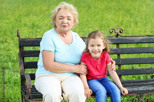 Cute little girl with grandmother sitting on bench in park © Pixel-Shot