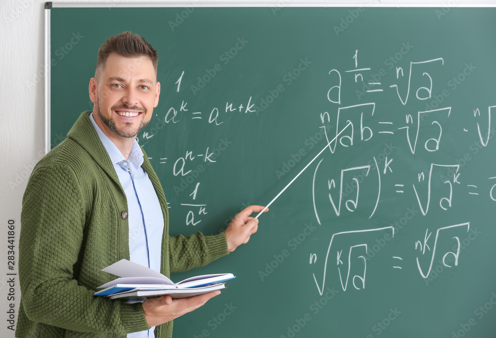 Handsome math teacher near blackboard in classroom - obrazy, fototapety, plakaty 