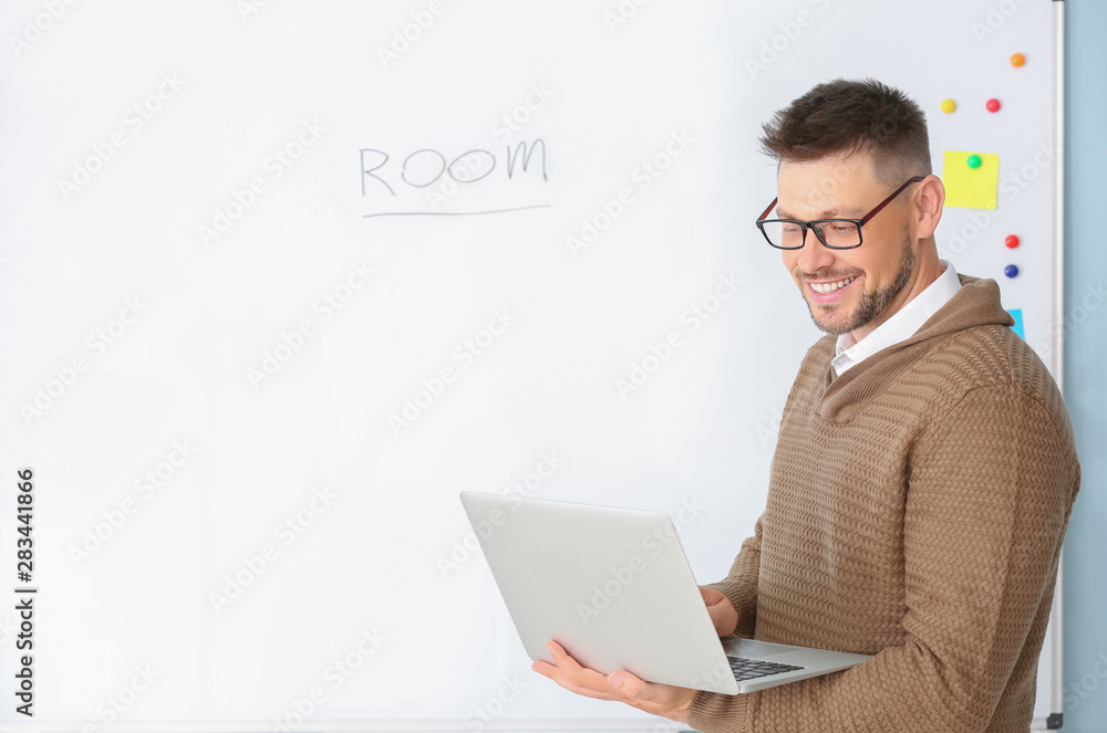 Handsome male teacher with laptop near blackboard in classroom Handsome male teacher with laptop near blackboard in classroom
