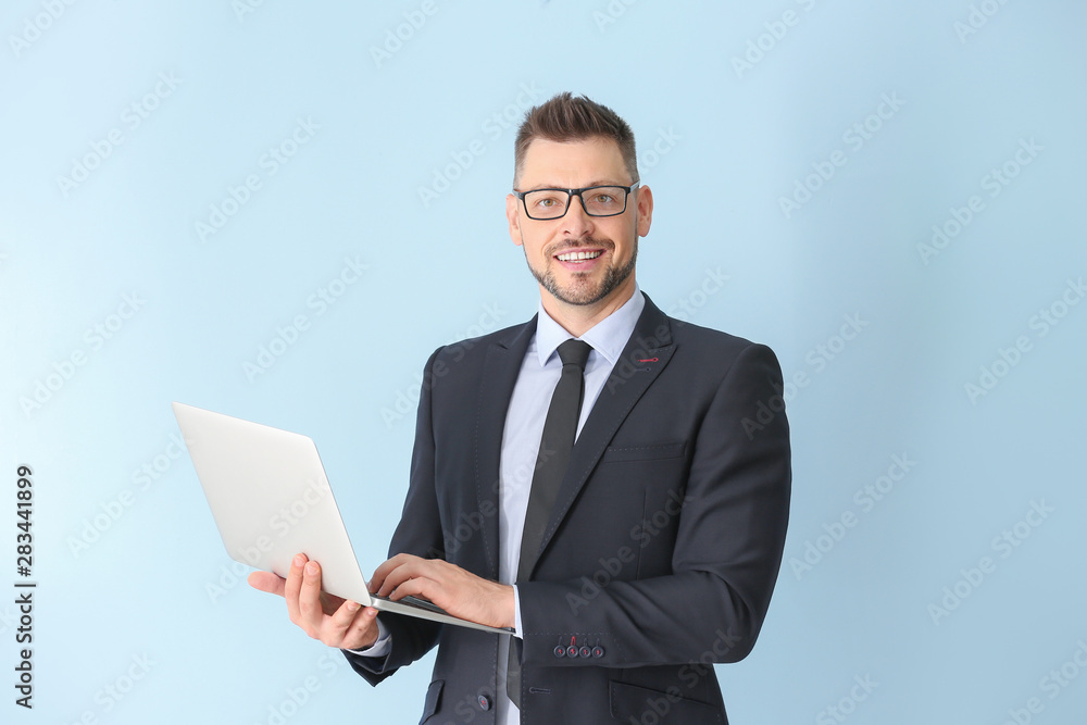 Handsome male teacher with laptop on light background