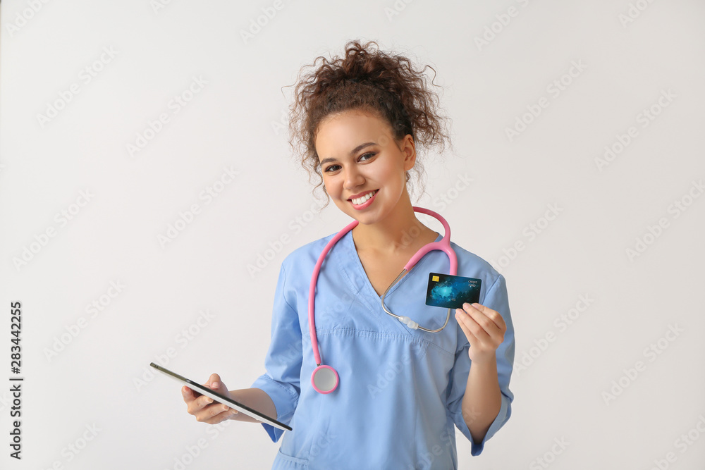 African-American doctor with credit card and tablet computer on light background African-American doctor with credit card and tablet computer on light background