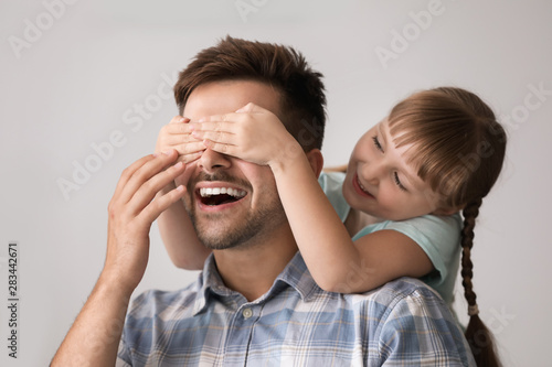 Happy little daughter covering eyes of her father at home