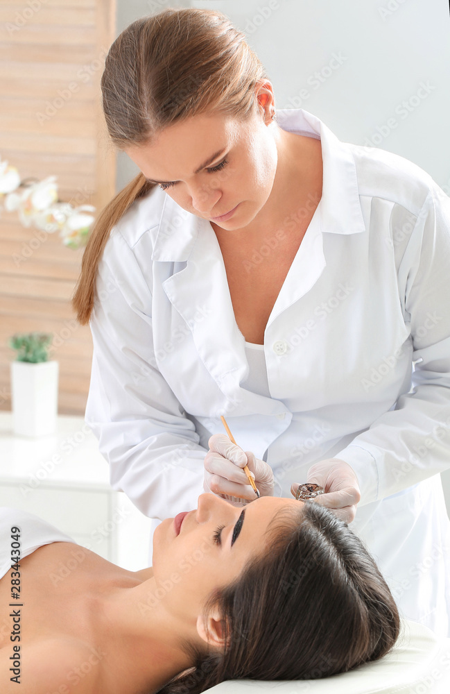 Fototapeta premium Young woman undergoing eyebrow correction procedure in beauty salon