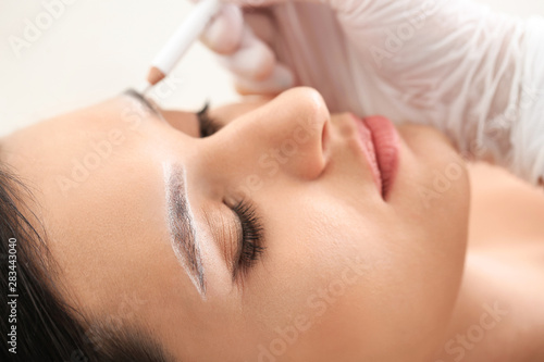 Young woman undergoing eyebrow correction procedure in beauty salon, closeup