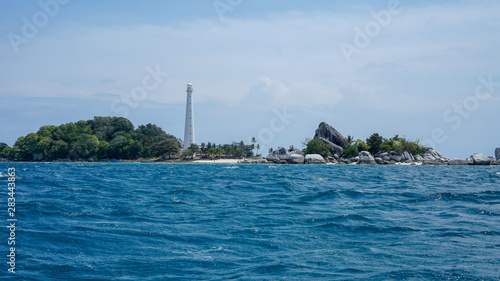 white lighthouse on the island with blue sea, big rocks and green trees © Reza Fahrizal