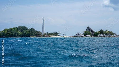 white lighthouse on the island with blue sea, big rocks and green trees