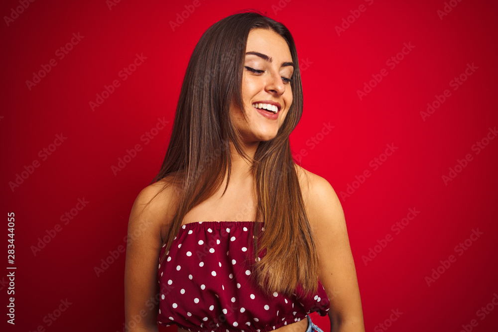 Young beautiful woman wearing casual t-shirt standing over isolated red background looking away to side with smile on face, natural expression. Laughing confident. Young beautiful woman wearing casual t-shirt standing over isolated red background looking away to side with smile on face, natural expression. Laughing confident.