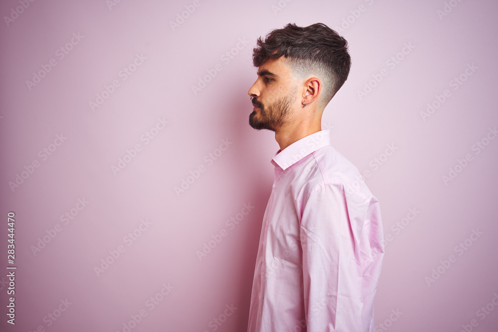 Young man with tattoo wearing shirt standing over isolated pink background looking to side, relax profile pose with natural face with confident smile. Young man with tattoo wearing shirt standing over isolated pink background looking to side, relax profile pose with natural face with confident smile.