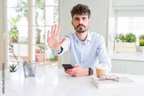 Young business man using smartphone sending a message with open hand doing stop sign with serious and confident expression  defense gesture