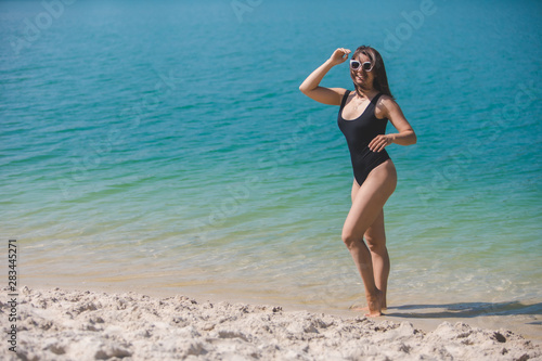smiling woman in sunglasses and black swimsuit in blue clear water