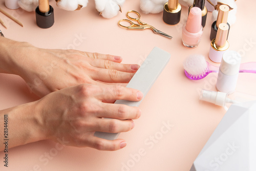 Nail care. Beautiful women hands making nails painted by pink delicate nail polish on a gentle background. Female hands near a set of professional manicure tools. Beauty care. Closeup manicure.