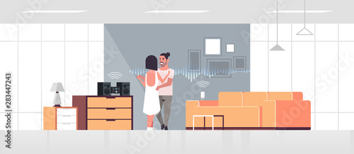 couple using Hi-Fi stereo system controlled by smart speaker voice recognition activated digital assistant smart home concept man woman dancing modern living room interior full length horizontal