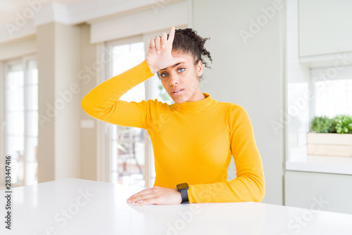 Beautiful african american woman with afro hair wearing a casual yellow sweater making fun of people with fingers on forehead doing loser gesture mocking and insulting.