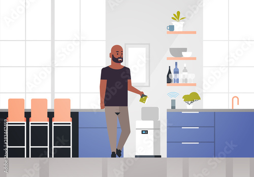 african american man putting trash in electronic recycling bin controlled by smart speaker voice recognition activated digital assistant concept modern kitchen interior horizontal full length