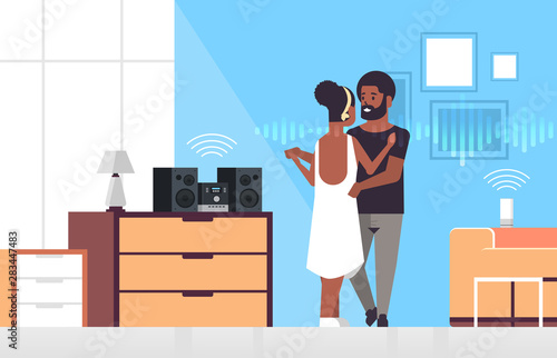 couple using Hi-Fi stereo system controlled by smart speaker voice recognition activated assistant smart home concept african american man woman dancing living room interior full length horizontal