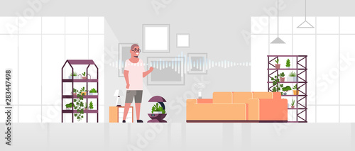 man using auto watering system controlled by smart speaker voice recognition activated digital assistant smart home concept modern living room interior flat full length horizontal