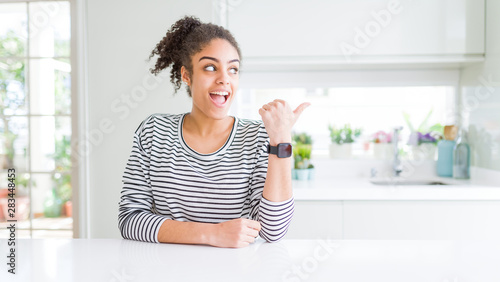 Beautiful african american woman with afro hair wearing casual striped sweater smiling with happy face looking and pointing to the side with thumb up.