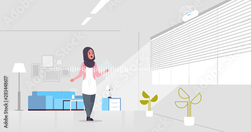 arab woman using smart speaker voice recognition activated digital assistant concept modern living room interior flat horizontal full length