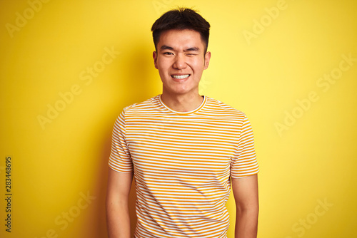 Young asian chinese man wearing t-shirt standing over isolated yellow background winking looking at the camera with sexy expression, cheerful and happy face.