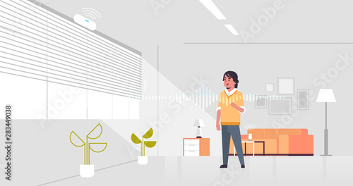 casual man using smart speaker voice recognition activated digital assistant concept modern living room interior flat horizontal full length