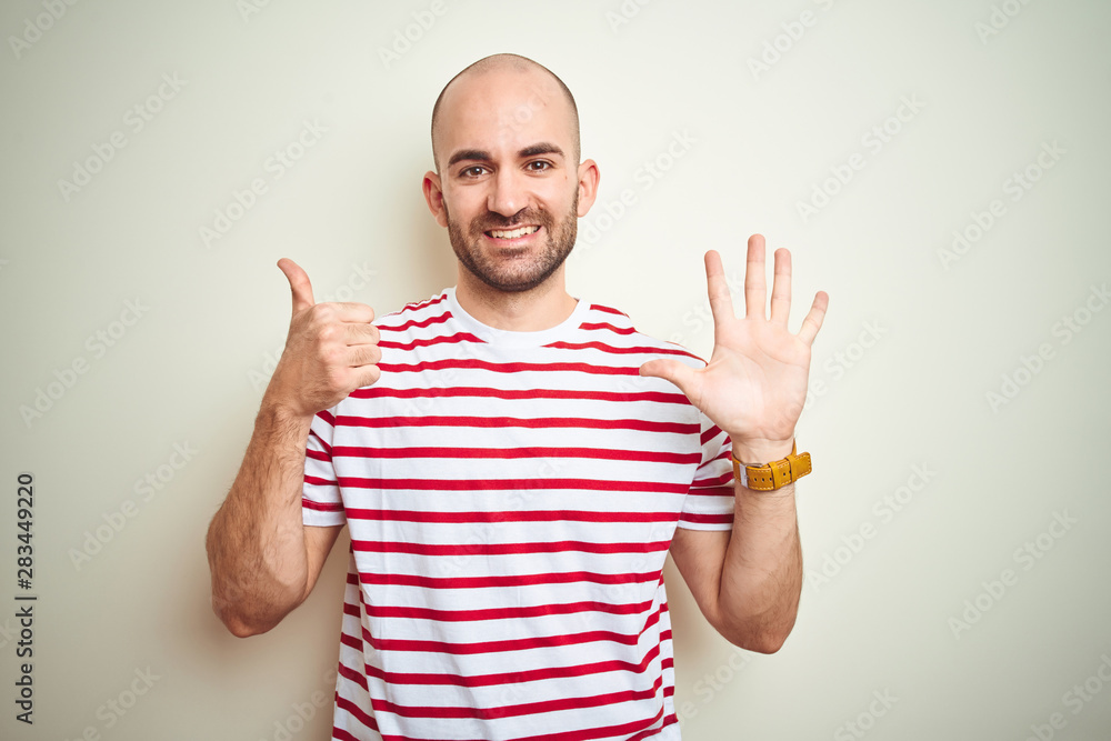 Naklejka premium Young bald man with beard wearing casual striped red t-shirt over white isolated background showing and pointing up with fingers number six while smiling confident and happy.
