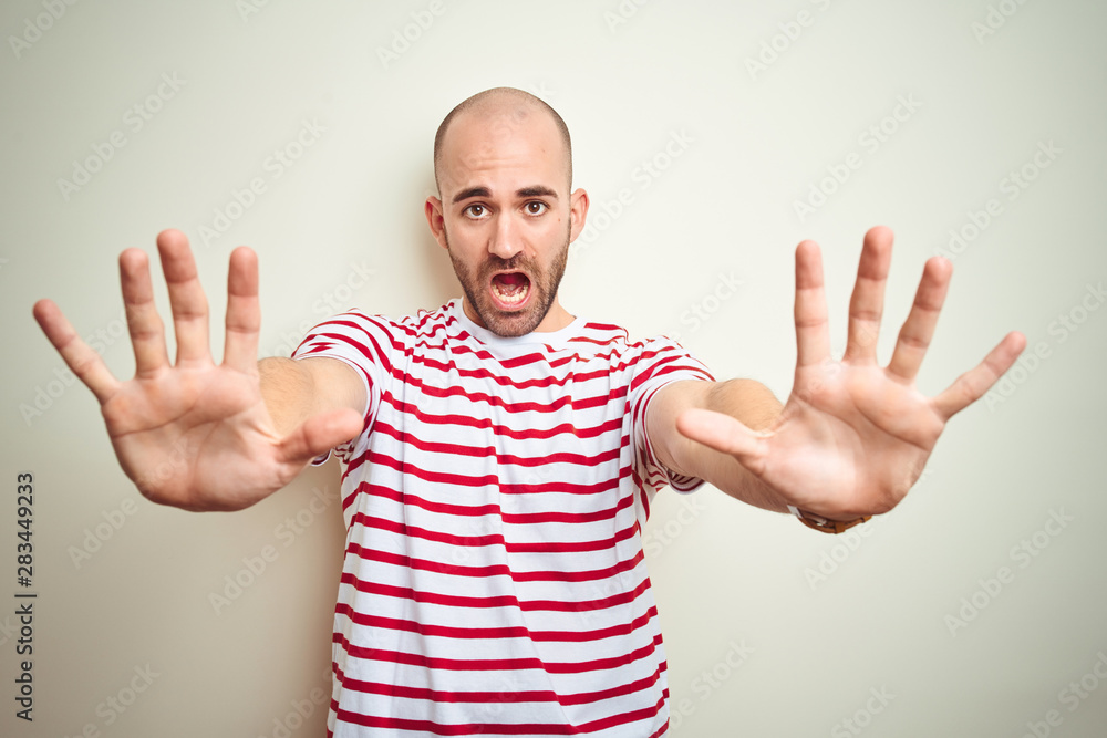 Fototapeta premium Young bald man with beard wearing casual striped red t-shirt over white isolated background doing stop gesture with hands palms, angry and frustration expression