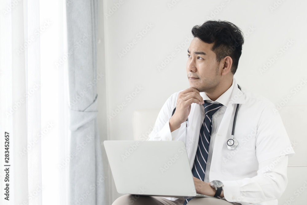 Asian doctor using laptop thinking and look out window, lifestyle concept.