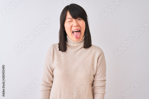 Young beautiful chinese woman wearing turtleneck sweater over isolated white background sticking tongue out happy with funny expression. Emotion concept. © Krakenimages.com