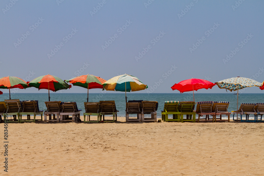 Row of covered wooden deck chairs with colorful umbrellas on the beach in GOA, India. Sea summer background. Holiday template.