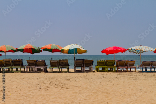 Row of covered wooden deck chairs with colorful umbrellas on the beach in GOA  India. Sea summer background. Holiday template.