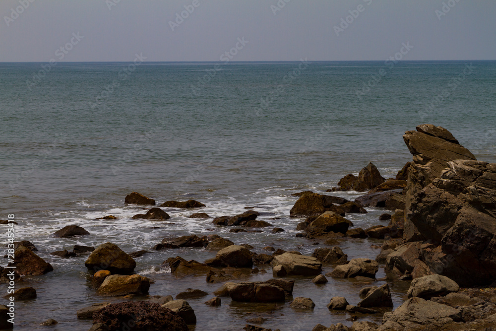 Rocky seashore with mist on the water. Natural scenery of dark day. Summer travel background. India, GOA, Arambol.