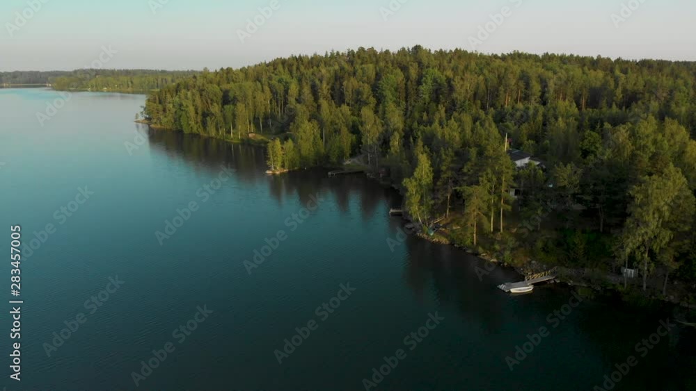 Aerial, descending, drone shot, panning around forest and a summerhouse, towards tranquil waters, on the coast of lake Hvittrask, on a sunny, summer evening, in Kirkkonummi, Uusimaa, Finland Aerial, descending, drone shot, panning around forest and a summerhouse, towards tranquil waters, on the coast of lake Hvittrask, on a sunny, summer evening, in Kirkkonummi, Uusimaa, Finland
