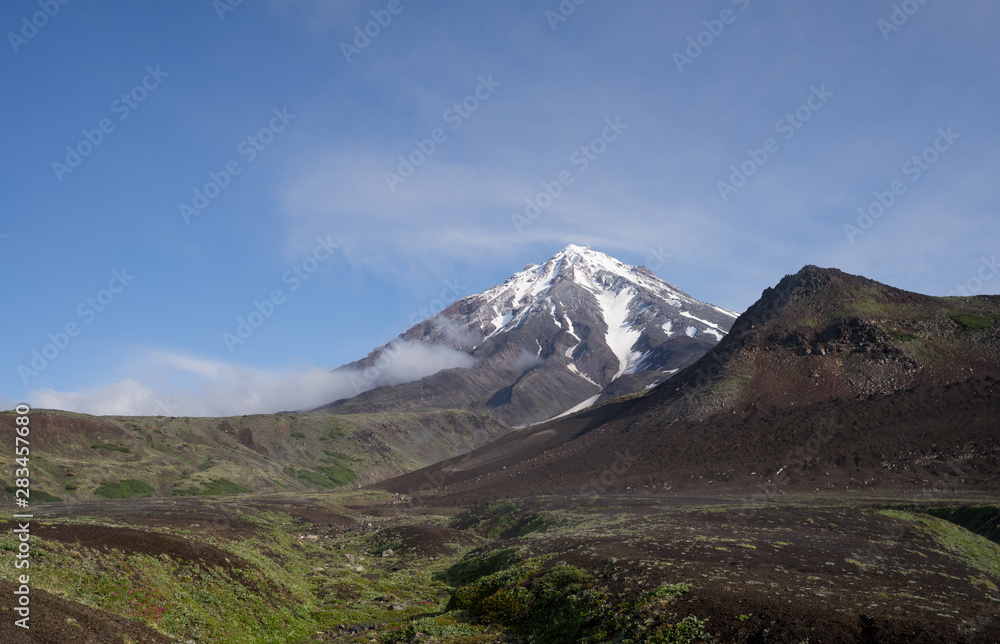 Symmetrical conus of Koryaksky (also known: Koryakskaya Sopka) surrounded by clouds. An active volcano in Kamchatka Peninsula in Russian Far East seen from neighbouring Avacha base camp. 