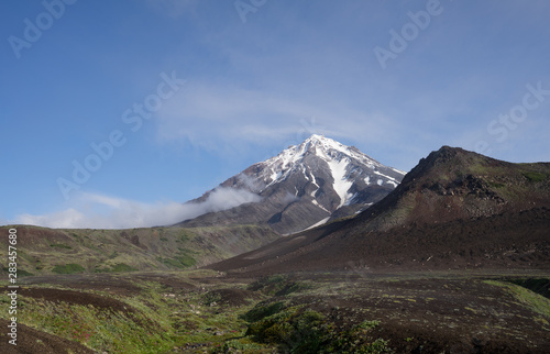 Symmetrical conus of Koryaksky (also known: Koryakskaya Sopka) surrounded by clouds. An active volcano in Kamchatka Peninsula in Russian Far East seen from neighbouring Avacha base camp. 