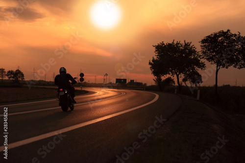 Motocyklista na tle zachodzącego słońca, droga szybkiego ruchu.