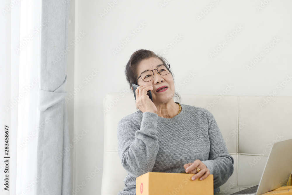 Asian senior woman taking order by phone ,online business with packaging and work at home concept. Asian senior woman taking order by phone ,online business with packaging and work at home concept.