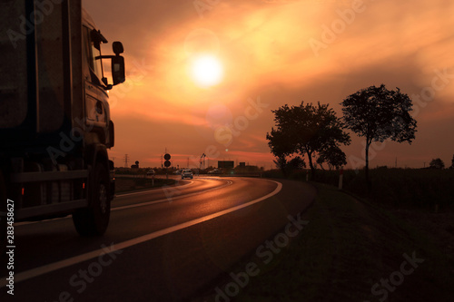 Samochód ciężarowy, tir na tle zachodzącego słońca, droga szybkiego ruchu. 