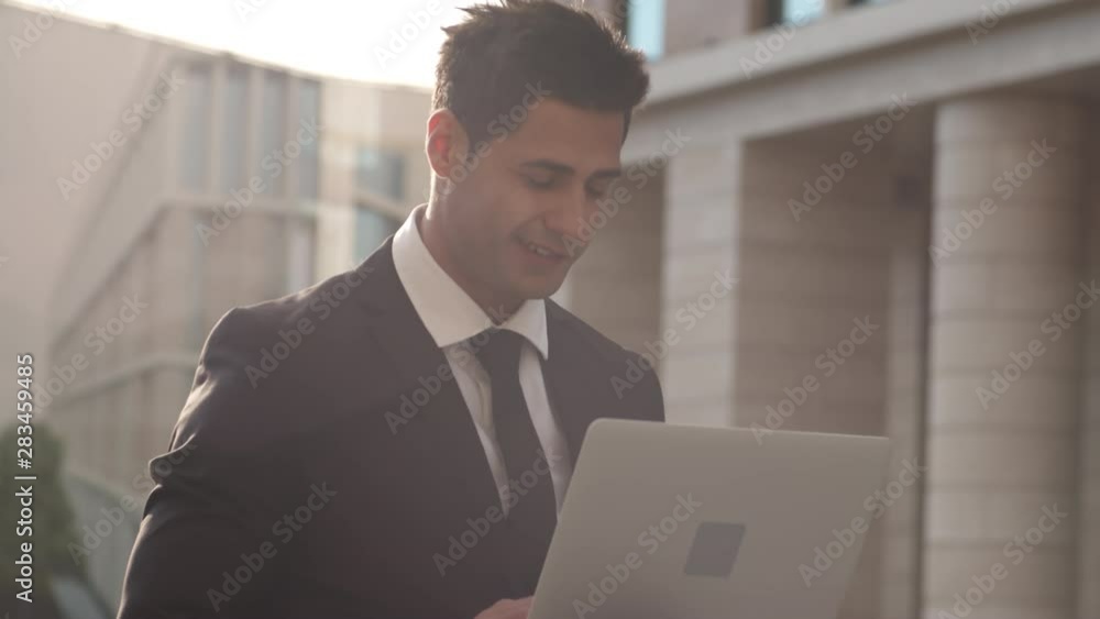 Close up of mixed-race businessman sitting outside with laptop and messaging with business partner Close up of mixed-race businessman sitting outside with laptop and messaging with business partner
