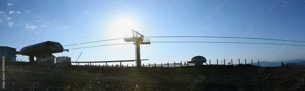 Panoramic view of the mechanism for lifting skiers in front of the autumn sun. Alps, Switzerland