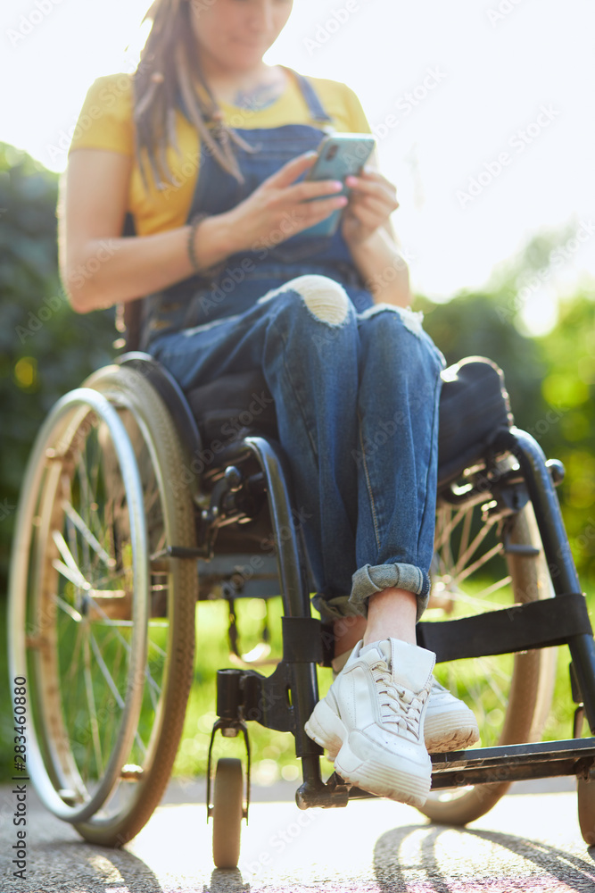 Obraz premium young attractive woman in wheelchair texting with her mobile phone, disability and employment concept. close up cropped photo. blurred background. free time, spare time