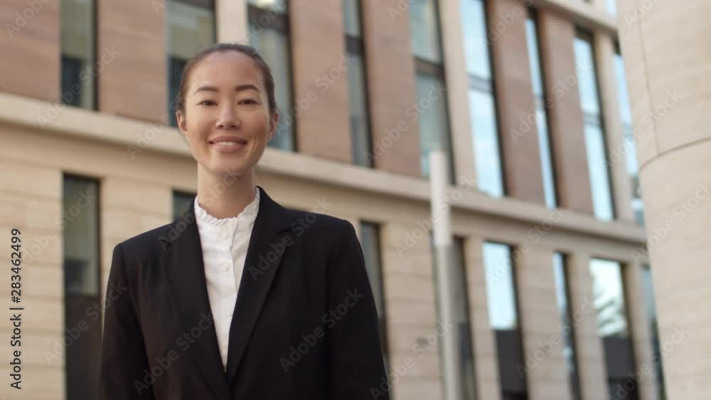 Low angle view of young Asian businesswoman wearing smart clothing looking aside, turning her head, looking at camera and smiling Low angle view of young Asian businesswoman wearing smart clothing looking aside, turning her head, looking at camera and smiling