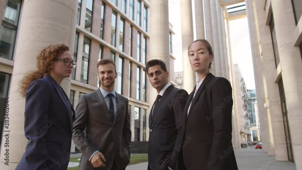 Tilt down of two diverse businesswomen talking to two elegant businessmen standing nearby in downtown and then looking at camera Tilt down of two diverse businesswomen talking to two elegant businessmen standing nearby in downtown and then looking at camera