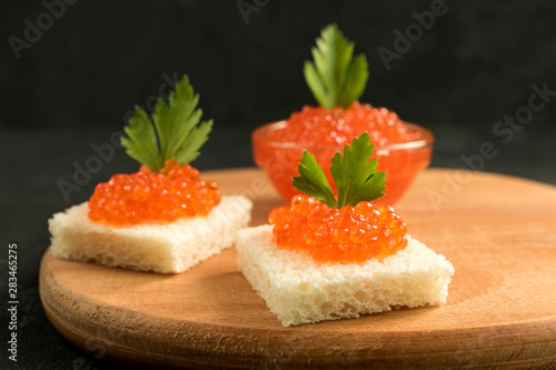 Delicious red caviar on wheat bread served with parseley on wooden desk.