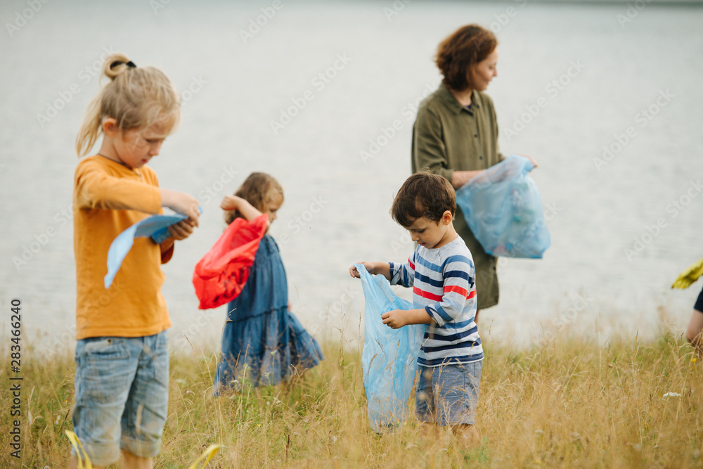 Mother with her kids collecting garbage on a meadow next to the river Mother with her kids collecting garbage on a meadow next to the river
