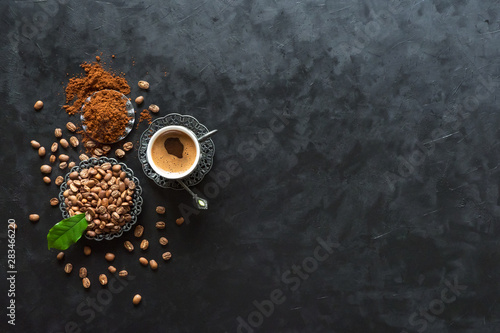 Cup of coffee and coffee beans with ground powder on black background, top view