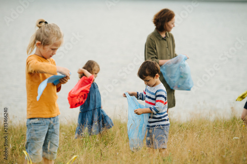 Fotografie Mother with her kids collecting garbage on a meadow next to the river