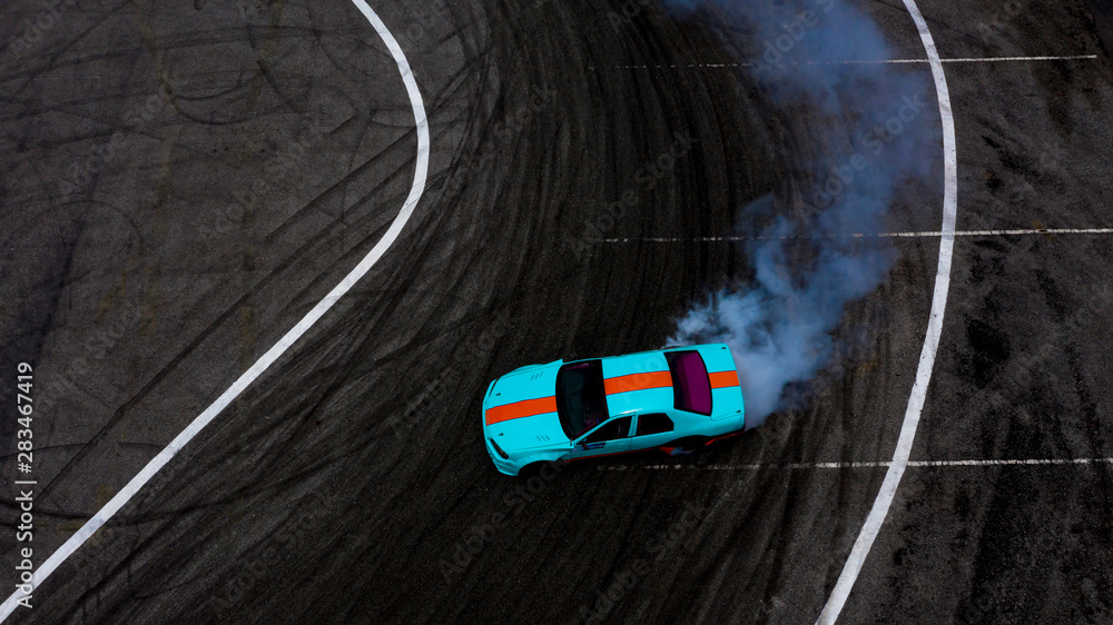 Aerial top view car drifting on asphalt race track with lots of smoke from burning tires.
