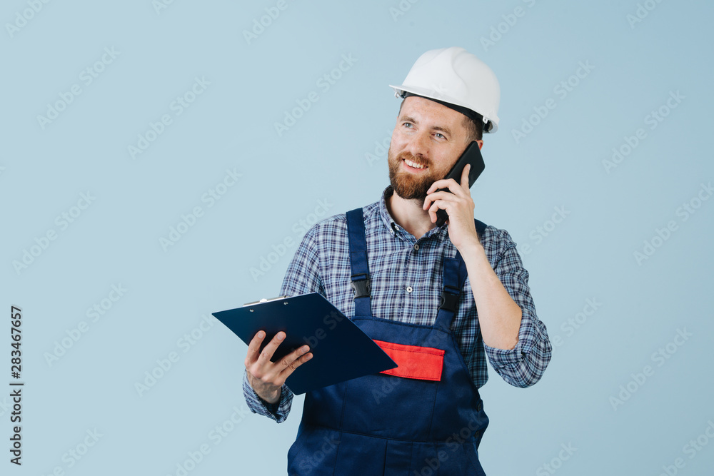 Happy construction worker in a white helmet and blue overalls with a phone Happy construction worker in a white helmet and blue overalls with a phone
