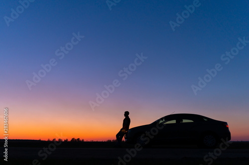 Silhouette of a man and a car on a background of a very beautiful sunset. Freedom and travel by car concept.