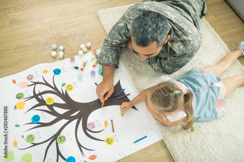 Fotografie Father and daughter lying on the floor and painting family tree